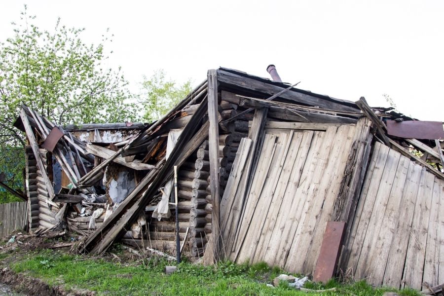 Collapsed wooden house with damaged roof and walls in a grassy yard after demolition or storm damage