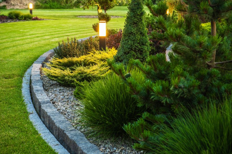 Curved stone garden border with shrubs, lawn, and path lights in a landscaped yard
